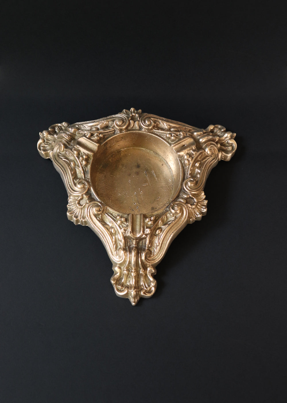 Vintage heavy cast brass ashtray is almost 2 kg in weight. The triangular body is ornamented in Baroque style with elaborate scrollwork, floral reliefs, acanthus leaves and rocaille shells. It has three integrated cigarette rests and a central bowl for the Ash. Should be from the mid 1900s, France.