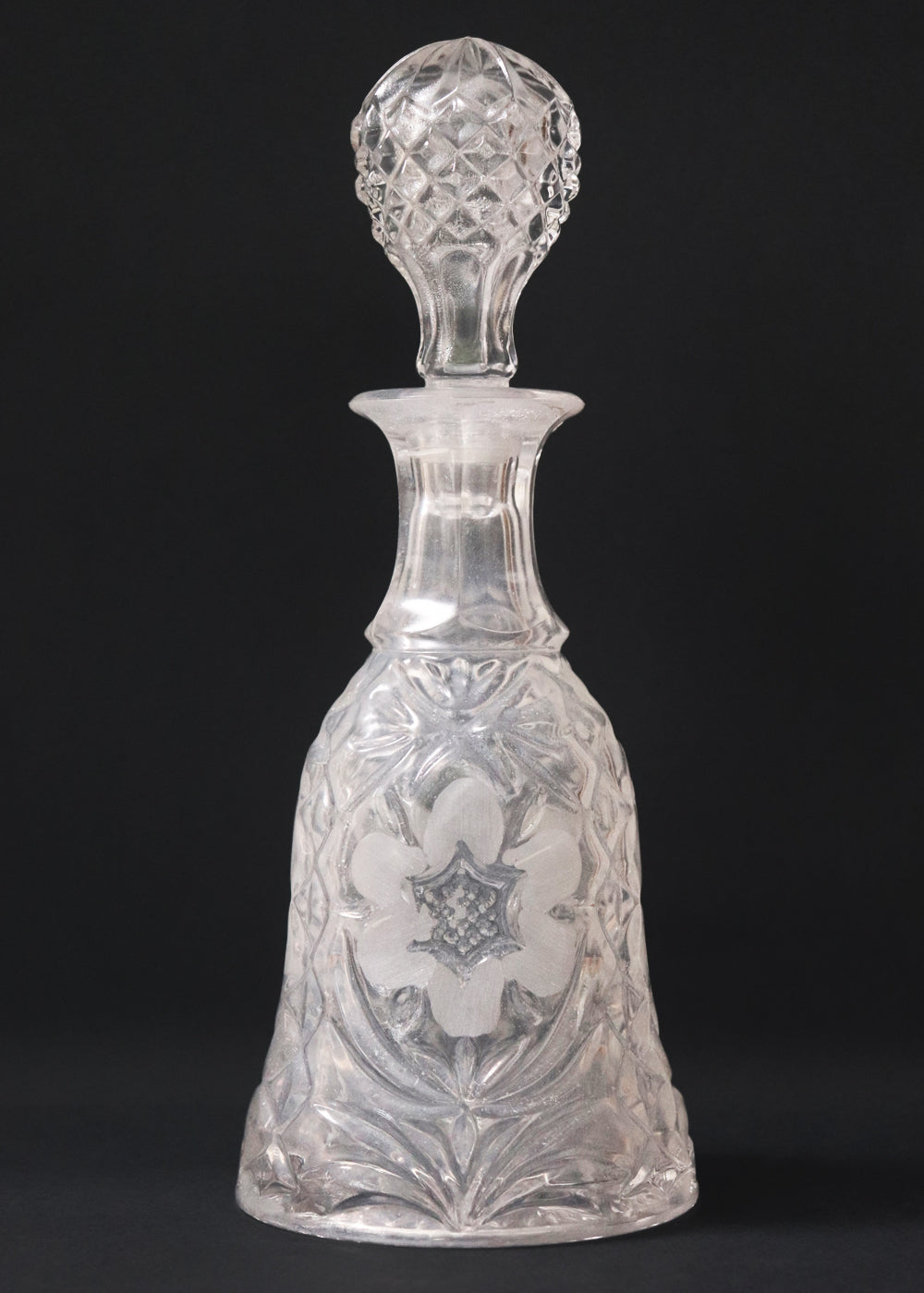 Vintage heavy cut glass decanter most likely meant for port wine. The bell shaped body is deeply facetted with patterns and has etched flowers around it. A diamond patterned ball shaped stopper sits atop the narrow neck. The crystal is somewhat cloudy but otherwise the decanter is in perfect condition. Should be from the mid 1900s, and most likely made in America.