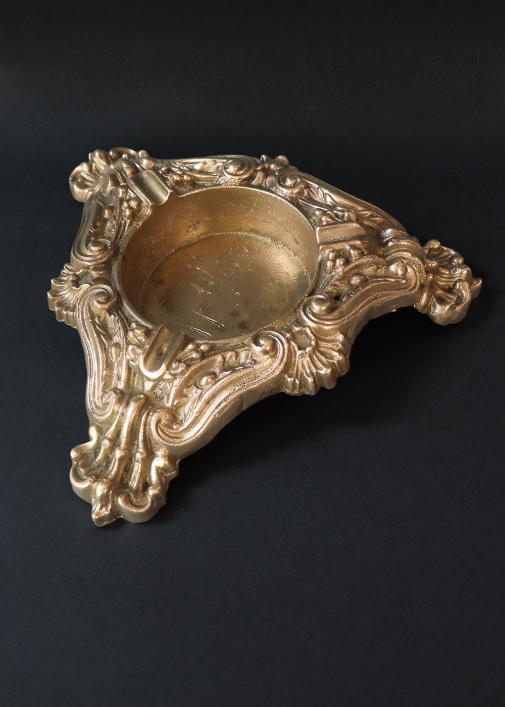 Vintage heavy cast brass ashtray is almost 2 kg in weight. The triangular body is ornamented in Baroque style with elaborate scrollwork, floral reliefs, acanthus leaves and rocaille shells. It has three integrated cigarette rests and a central bowl for the Ash. Should be from the mid 1900s, France.