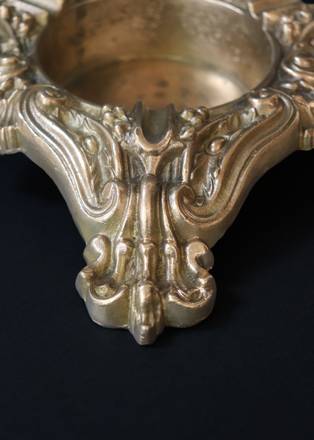 Vintage heavy cast brass ashtray is almost 2 kg in weight. The triangular body is ornamented in Baroque style with elaborate scrollwork, floral reliefs, acanthus leaves and rocaille shells. It has three integrated cigarette rests and a central bowl for the Ash. Should be from the mid 1900s, France.