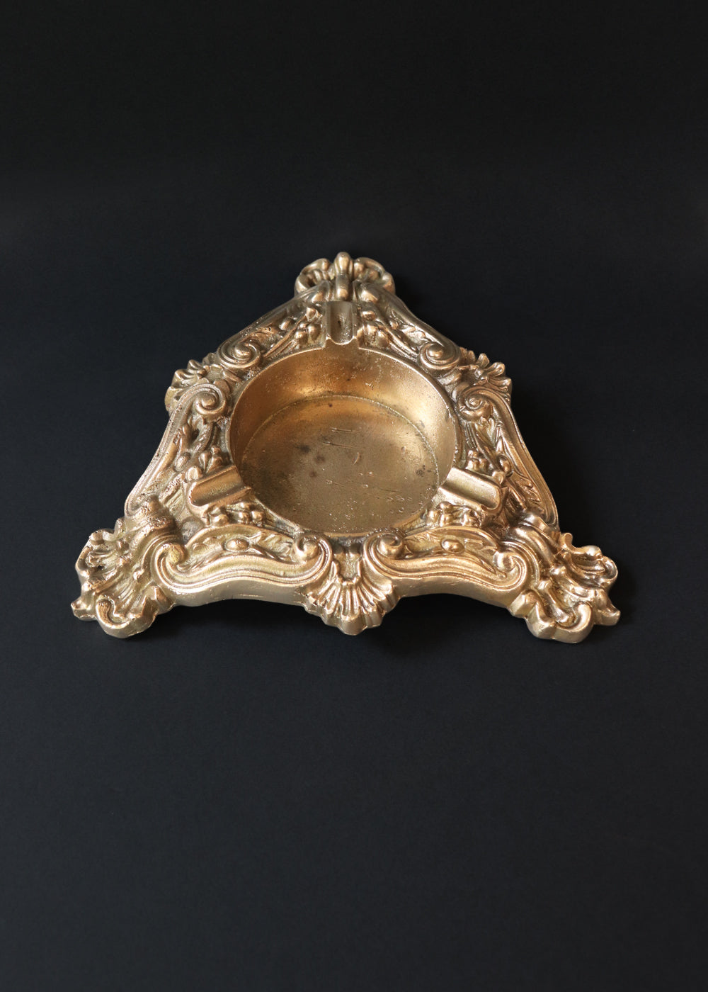 Vintage heavy cast brass ashtray is almost 2 kg in weight. The triangular body is ornamented in Baroque style with elaborate scrollwork, floral reliefs, acanthus leaves and rocaille shells. It has three integrated cigarette rests and a central bowl for the Ash. Should be from the mid 1900s, France.