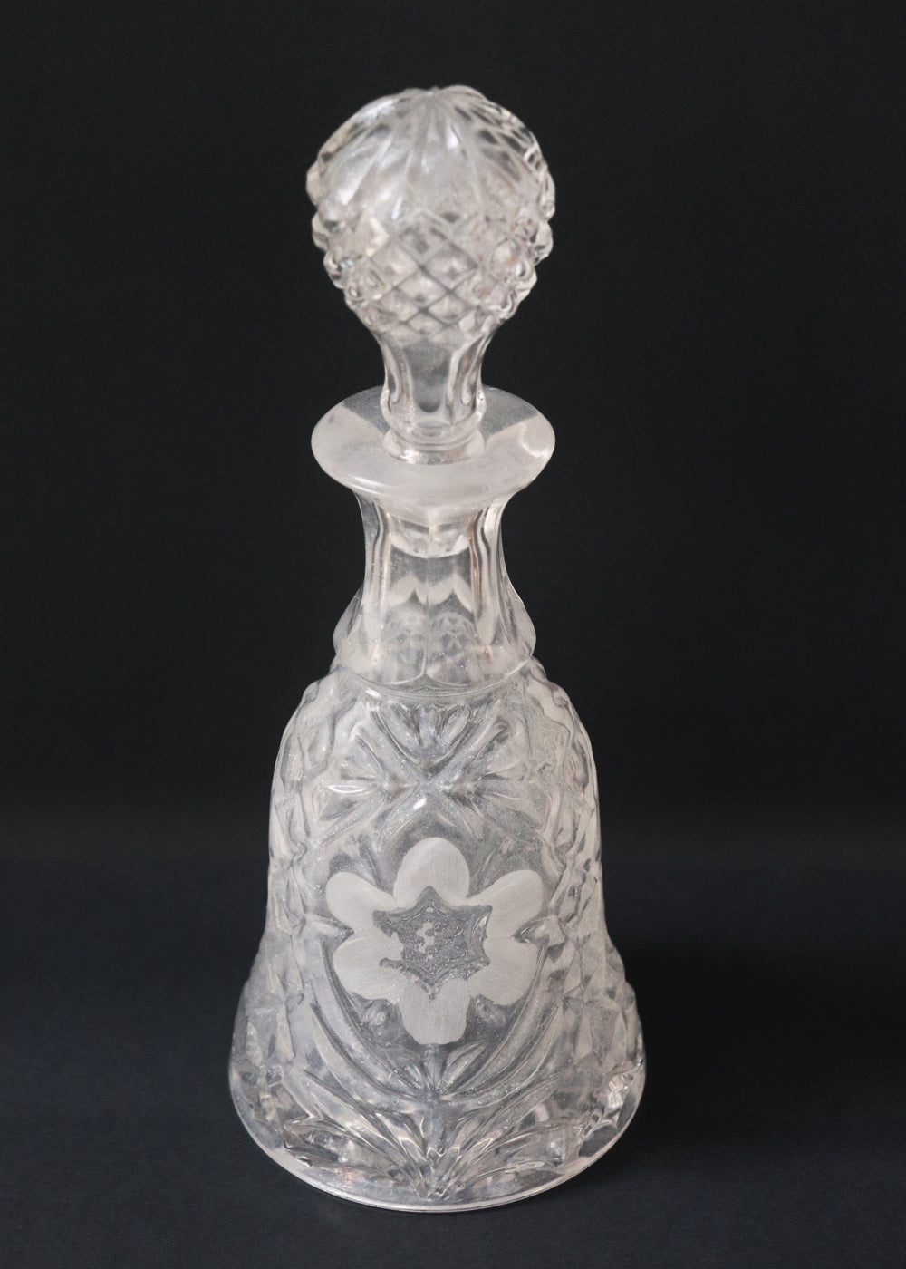Vintage heavy cut glass decanter most likely meant for port wine. The bell shaped body is deeply facetted with patterns and has etched flowers around it. A diamond patterned ball shaped stopper sits atop the narrow neck. The crystal is somewhat cloudy but otherwise the decanter is in perfect condition. Should be from the mid 1900s, and most likely made in America.