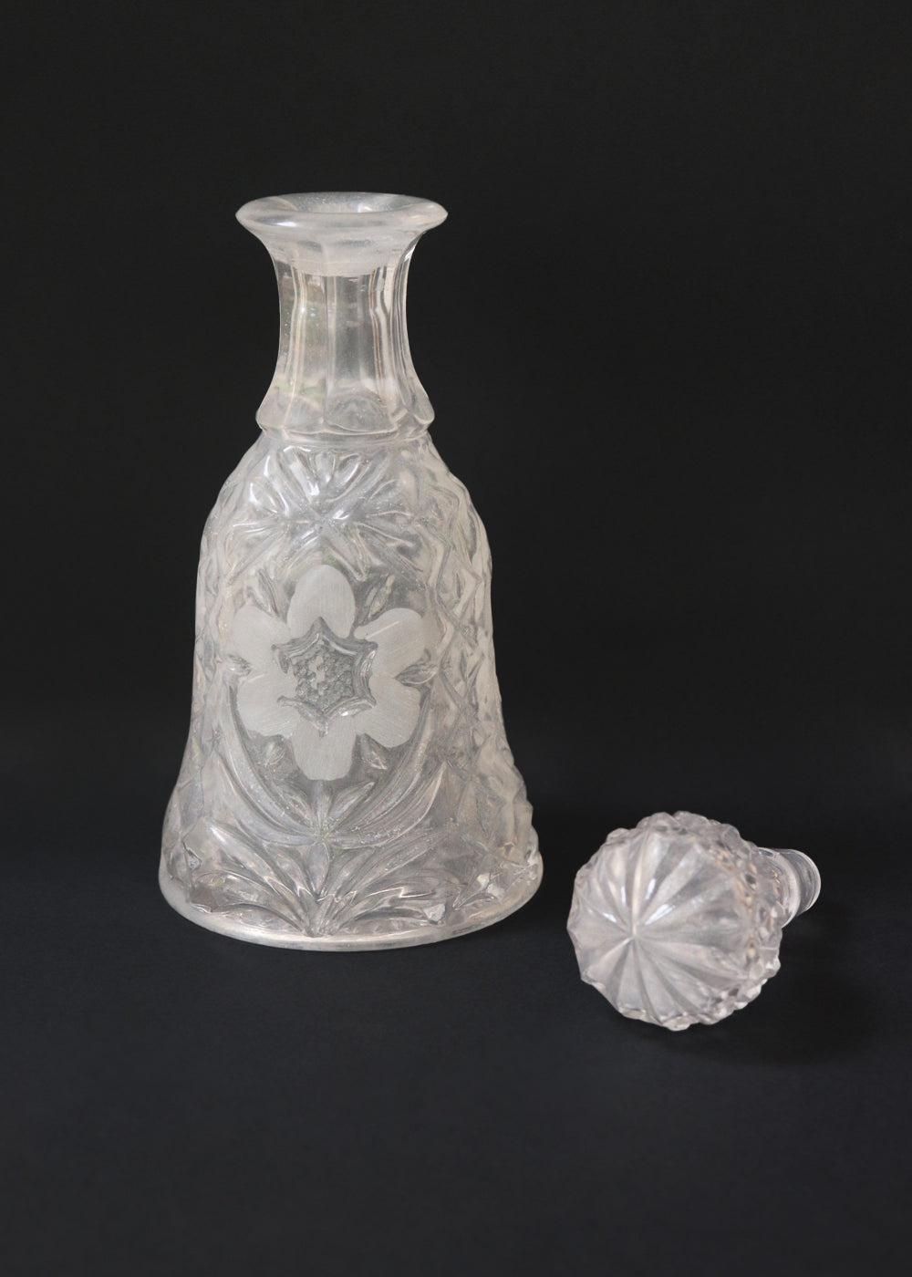 Vintage heavy cut glass decanter most likely meant for port wine. The bell shaped body is deeply facetted with patterns and has etched flowers around it. A diamond patterned ball shaped stopper sits atop the narrow neck. The crystal is somewhat cloudy but otherwise the decanter is in perfect condition. Should be from the mid 1900s, and most likely made in America.