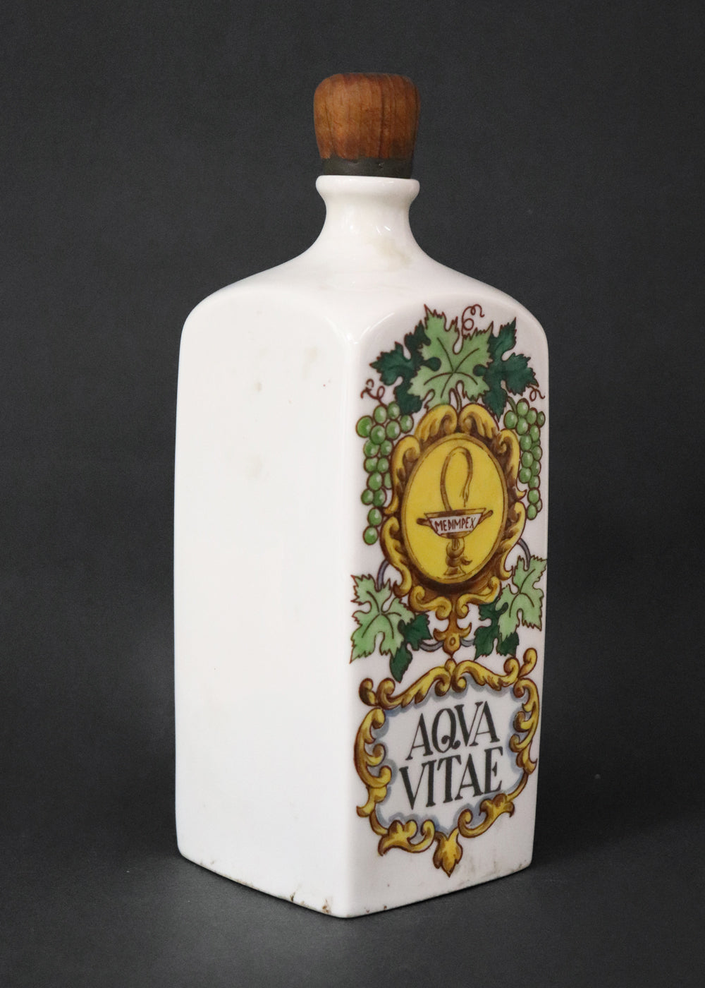 Vintage collectible Hollóházi porcelain bottle specially designed for "Aqua Vitae," which is an old Latin term for "water of life" typically referring to early distilled spirits. Medimpex, who’s name is on a medallion framed with scrolls was a well-known Hungarian/Eastern European pharmaceutical and medical distribution company. The bottle features a green and gold grapevine motifs framing a cartouche with the words "AQVA VITAE" boldly painted in the center. The wooden stopper is in perfect condition. Holló