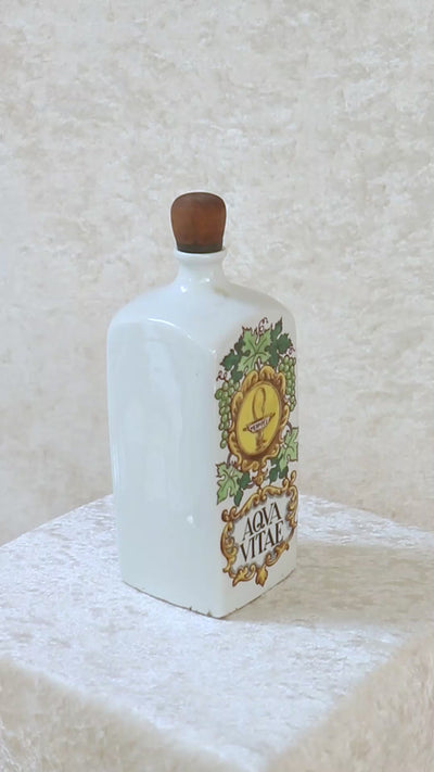 Vintage collectible Hollóházi porcelain bottle specially designed for "Aqua Vitae," which is an old Latin term for "water of life" typically referring to early distilled spirits. Medimpex, who’s name is on a medallion framed with scrolls was a well-known Hungarian/Eastern European pharmaceutical and medical distribution company. The bottle features a green and gold grapevine motifs framing a cartouche with the words "AQVA VITAE" boldly painted in the center. The wooden stopper is in perfect condition. Holló