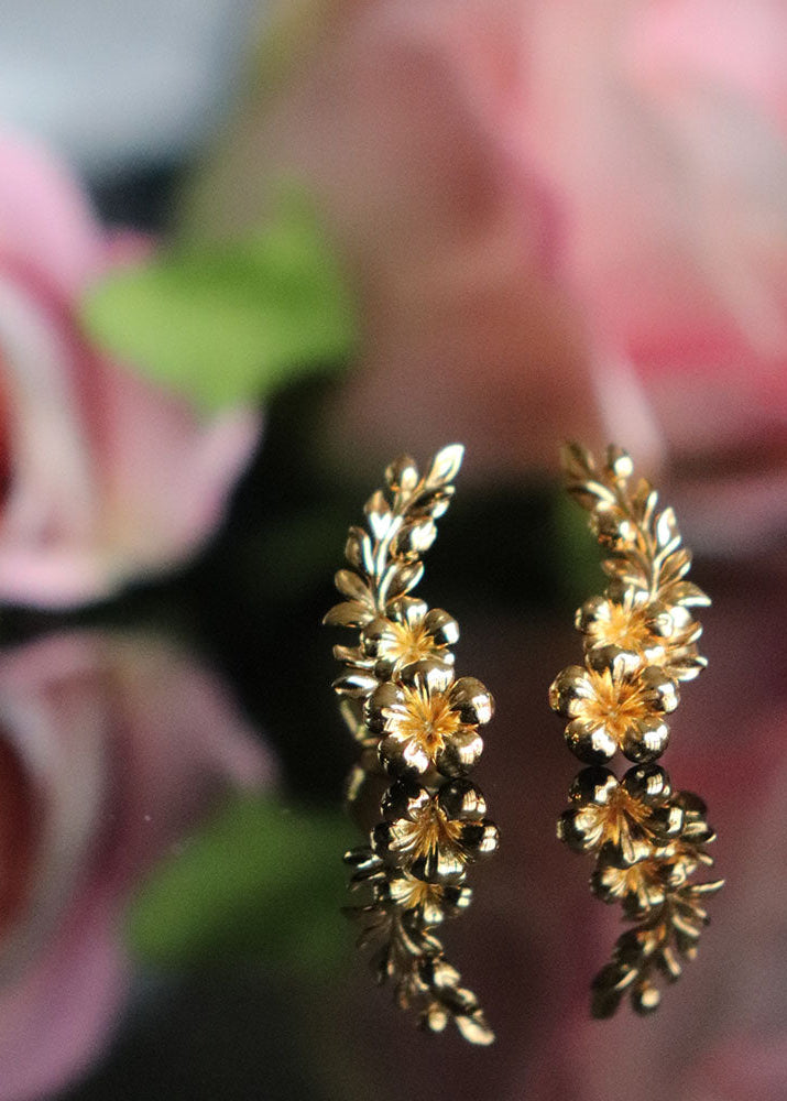 A pair of gold-toned floral stud earrings with leafy sprigs and small flower details
